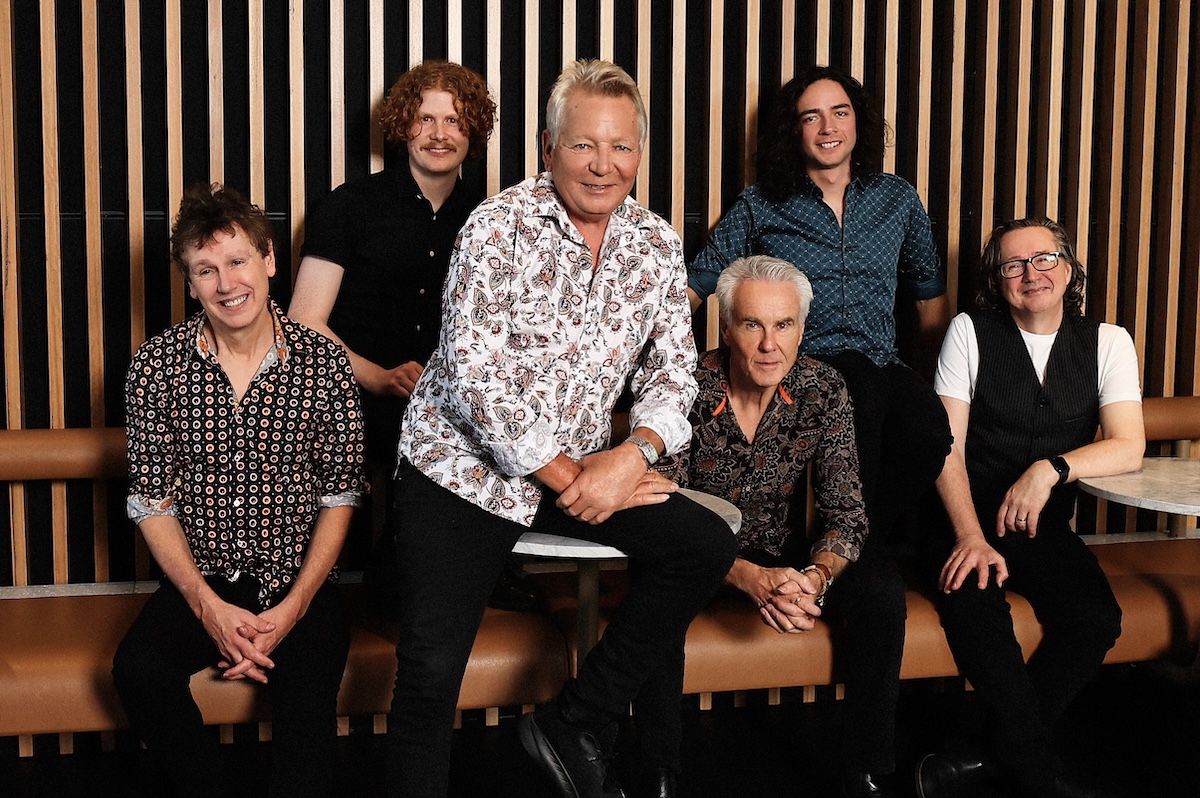 Australian rock band Icehouse photo by Glenn Nicholls, featuring Iva Davies and band members sitting in front of a wood-panel wall portrait.